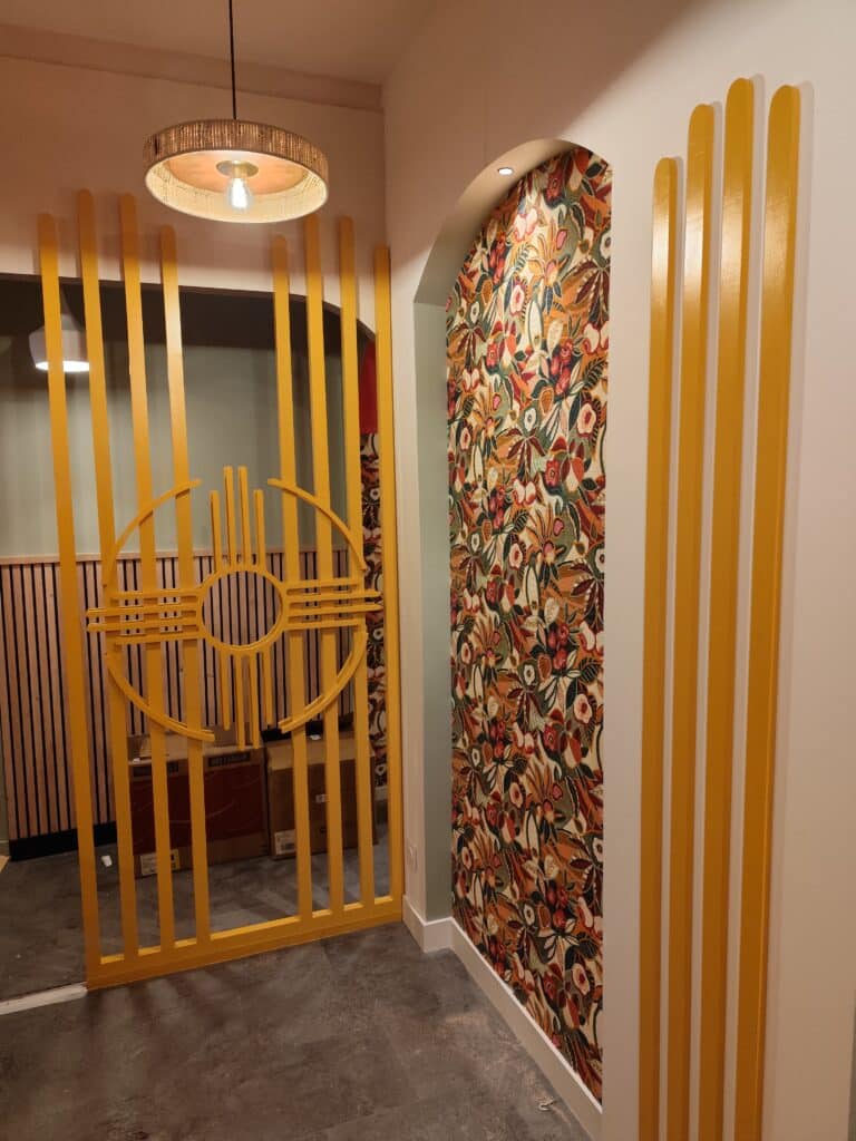 Design intérieur moderne: cloison jaune & motifs floraux muraux Décoration intérieure moderne avec cloison jaune à motifs circulaires, arche murale tapissée de motifs floraux vifs et lattes verticales jaunes.