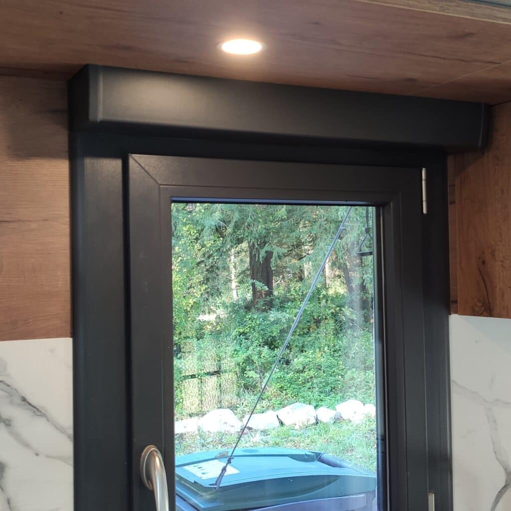 Fenêtre moderne avec store intégré : design bois, vue nature Fenêtre/porte moderne noire avec store intégré. Vue sur forêt luxuriante. Plafond en bois avec spot allumé et comptoir marbre blanc.