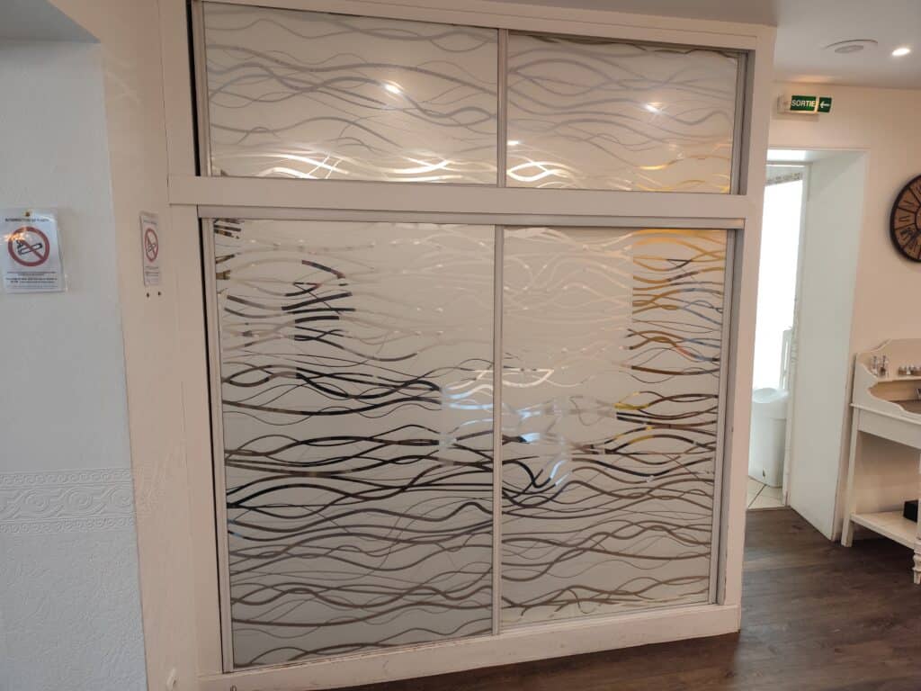 Cloison Vitrée Décorative à Motif Vagues Givrées Cloison vitrée à motifs de vagues givrées séparant deux pièces. Signes Interdiction de fumer et Sortie visibles.